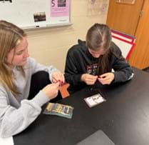 A photo showing two high school students using notecards and copper tape to build a logic gate. A photo showing two high school students using notecards and copper tape to build a logic gate.