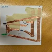 A photo of a NOT gate built on a piece of cardboard from a cereal box cut to the size of a notecard. The gate is built using copper tape, three resistors, two transistors and an LED. There is also masking tape used to separate layers of the copper tape to prevent short circuits. There are two places in the circuit where gaps are left between pieces of copper tape to create the switches in their open states. A photo of a NOT gate built on a piece of cardboard from a cereal box cut to the size of a notecard. The gate is built using copper tape, three resistors, two transistors and an LED. There is also masking tape used to separate layers of the copper tape to prevent short circuits. There are two places in the circuit where gaps are left between pieces of copper tape to create the switches in their open states.