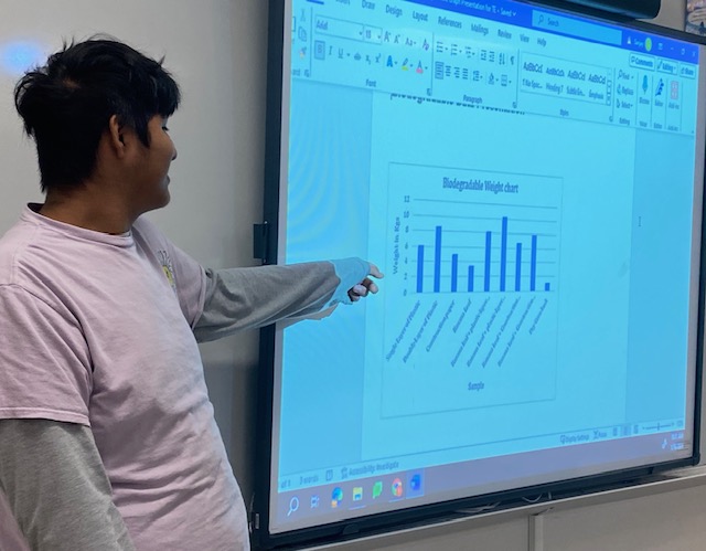 A photo of a student pointing to a display and explaining the experiment results in graph form.