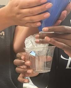 A photo showing student hands directing a filtered funnel tip into a plastic cup.