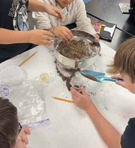 A photo showing students using common household items to separate potting soil into its components.