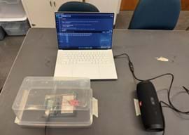 A photo of a complete sound insulation experiment setup. A laptop displays code, controlling a sound detection circuit (Arduino and breadboard) enclosed in a plastic container, while a Bluetooth speaker provides the sound source. A photo of a complete sound insulation experiment setup. A laptop displays code, controlling a sound detection circuit (Arduino and breadboard) enclosed in a plastic container, while a Bluetooth speaker provides the sound source.