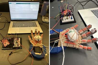 A photo of three cardboard hand designs, along with an Arduino circuit board, sitting on a table. The hands are connected by wires to the circuit. A photo of three cardboard hand designs, along with an Arduino circuit board, sitting on a table. The hands are connected by wires to the circuit.