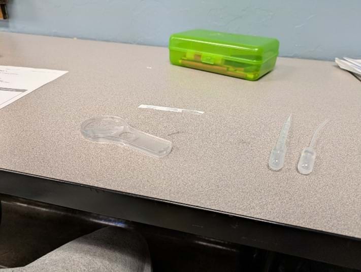 A photo showing a strip of Teflon tape with some water drops along with two pipettes and a magnifying glass on a worktable. A photo showing a strip of Teflon tape with some water drops along with two pipettes and a magnifying glass on a worktable.