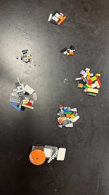 A photo showing various colors and shapes of LEGO pieces sorted and arranged into groups. There are seven groups of LEGO pieces on the table; the pieces within each pile look similar in size. 