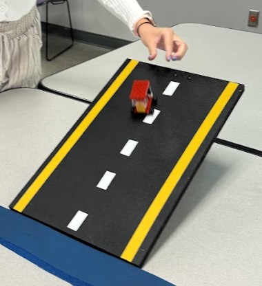 A photo of a student sending a completed plastic brick car down the ramp test. A photo of a student sending a completed plastic brick car down the ramp test.