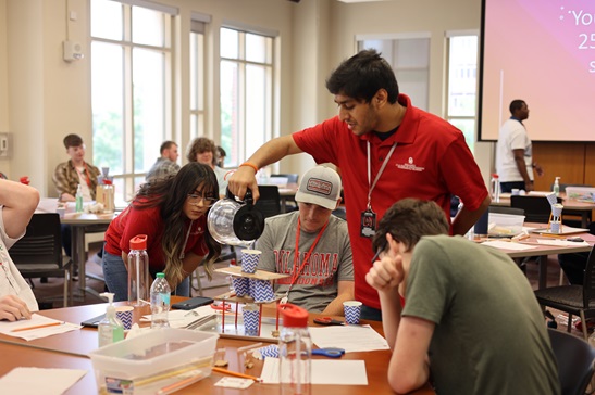 A photo of three students watching an instructor pour water into their machine for testing. 