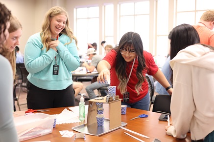 A photo of three students gathered around a table as one student pours water into the completed Gatorade machine. 