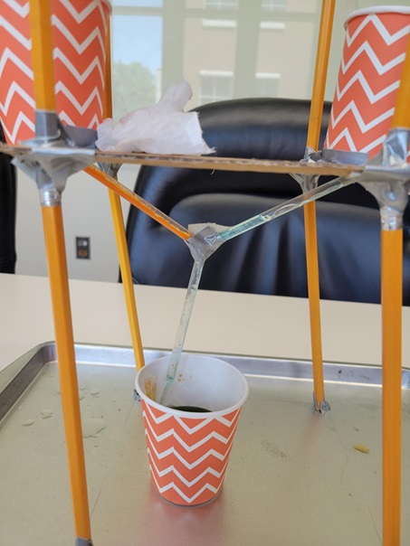 Picture of two cups supported by multiple unsharpened pencils above a single cup into which Gatorade powders and water flows. 