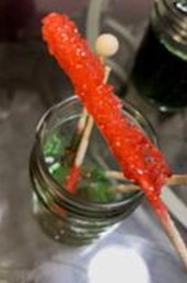 A photo of the end result of the at-home experiment, including a red sugar rock candy in the first plane and four more sugar rock candies of different colors resting in a glass container. 