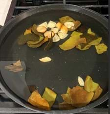 A photo of avocado skins, cut into pieces, boiling in a black pan filled with water on a stove. 