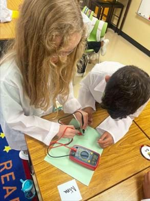 A photo showing two students testing the conductive glass using a multimeter.