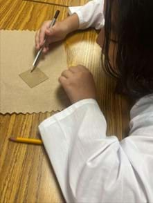 A photo showing a student coloring one side of the conductive glass with a pencil.