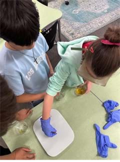 A photo showing three students weighing a gummy prototype on a gram scale. A photo showing three students weighing a gummy prototype on a gram scale.